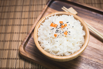 White rice in wooden bowl and chopsticks with sesame seeds and carrot on wood board