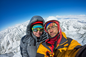 Fototapeta na wymiar Selfie couple climber in helmet and down jacket stand on top of mountain