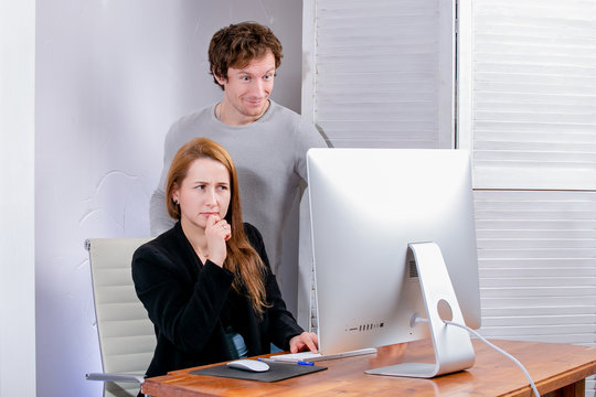 Portrait of young successful woman and man at office. They look at the display in surprise. Black Friday or Cyber Monday. Browsing or selecting items, making a deal, online shopping, good mood