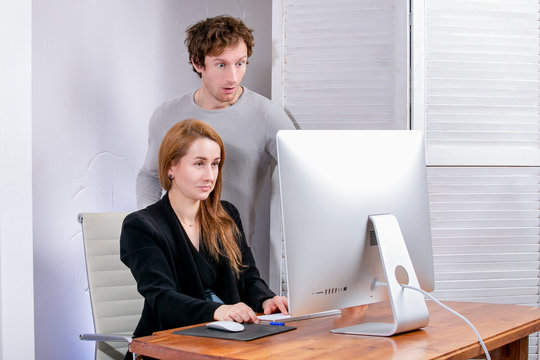Portrait of young successful woman and man at office. They look at the display in surprise. Black Friday or Cyber Monday. Browsing or selecting items, making a deal, online shopping, good mood