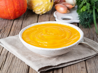 Delicious yellow pumpkin cream soup on dark gray old rustic wooden table, side view