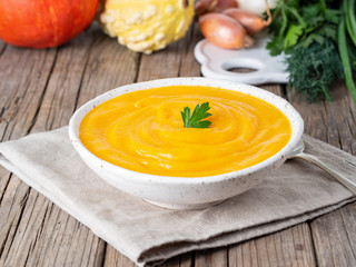Delicious pumpkin cream soup with parsley on dark gray old rustic wooden table, side view