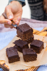 Woman hands take with fork vegan chocolate sweet brownie cake. Pumpkin, cacao powder, Iranian dates. No bake. Vegetarian raw dessert piece. Paleo diet. Healthy food