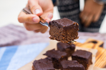 Woman hands take with fork vegan chocolate sweet brownie cake. Pumpkin, cacao powder, Iranian dates. No bake. Vegetarian raw dessert piece. Paleo diet. Healthy food