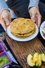 Woman hands holds, take chapati whole wheat grain flat bread. Indian traditional food. Served with avocado sauce, tomato sauce, fresh vegetables salad. Vegan vegetarian healthy paleo diet