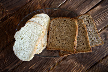 Slices of black and white bread in a glass plate on a light wooden surface