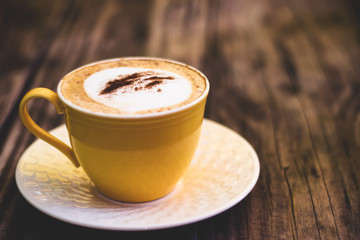 Cappuccino coffee in yellow cup on wooden table. Vintage tone