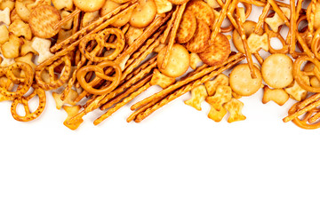 A photo of an assortment of salt crackers, sticks, pretzels, and fishes, shot from the top on a white background with copy space. Salty party snacks mix
