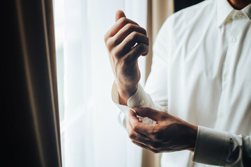 Naklejka premium A man fastens with a cufflink on the cuff of the sleeve of a luxurious white shirt. Close up of a man hand wearing a white shirt and cufflinks. Captures the groom cufflinks