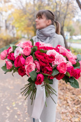Big luxury bright bouquet in the hands of a cute girl. One hundred garden roses, varieties of David Austin. Three kinds of bright pink, scarlet and pastel colors. Autumn leaves in the Park.