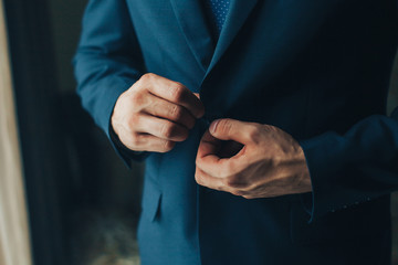 Buttoning a jacket hands close up. Stylish man in suit fastens buttons and straightens his jacket preparing to go out. Preparing for a wedding