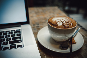 A cup of cappuccino coffee or latte coffe in a white cup with laptop on table. Royalty high quality free stock photo of drink capuccino or latte coffe with laptop for working in office