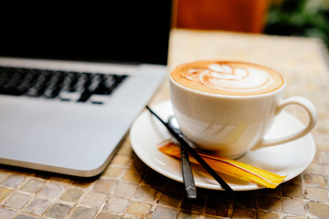 A cup of capuchino coffee or latte coffe in a white cup with laptop on table. Royalty high quality free stock photo of drink capuchino or latte coffe with laptop for working in office