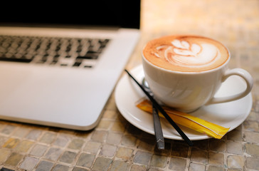 A cup of cappuccino coffee with laptop on table. Royalty high quality free stock image of capuccino coffee with laptop for working in a coffee shop. Beautiful workspace with retro and vintage style  