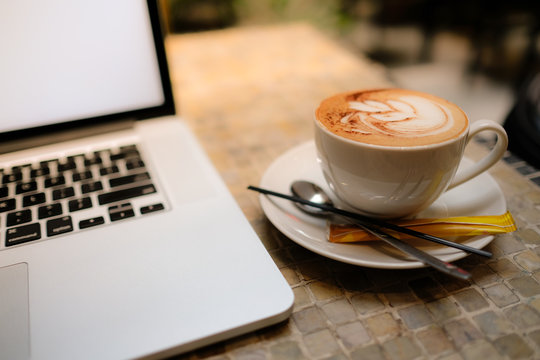 A cup of cappuccino coffee or chocolate cacao in a white cup with laptop on table. Royalty high quality free stock photo of drink capuccino or latte coffe with laptop for working in office