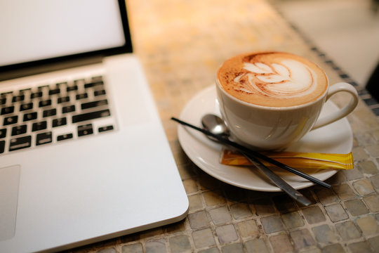 A cup of cappuccino coffee with laptop on table. Royalty high quality free stock image of capuccino coffee with laptop for working in a coffee shop. Beautiful workspace with retro and vintage style  