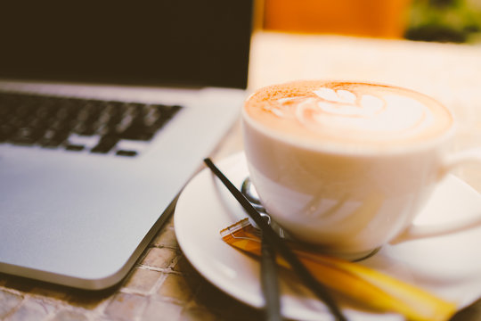 A cup of cappuccino coffee with laptop on table. Royalty high quality free stock image of capuccino coffee with laptop for working in a coffee shop. Beautiful workspace with retro and vintage style