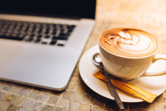 A cup of cappuccino coffee or latte coffe in a white cup with laptop on table. Royalty high quality free stock photo of drink capuccino or latte coffe with laptop for working in office
