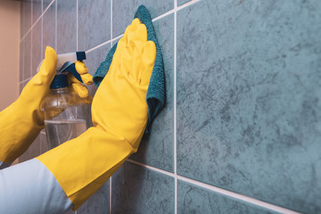 a woman with a rubber yellow glove wipes the tiles in the kitchen with a cloth