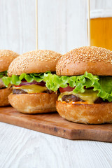 Homemade cheeseburgers and glass of beer on white wooden background, side view. Closeup.