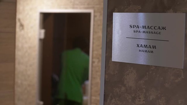 Close up plate with the words "spa massage". Through doorway you can see back of a masseuse who is massaging.