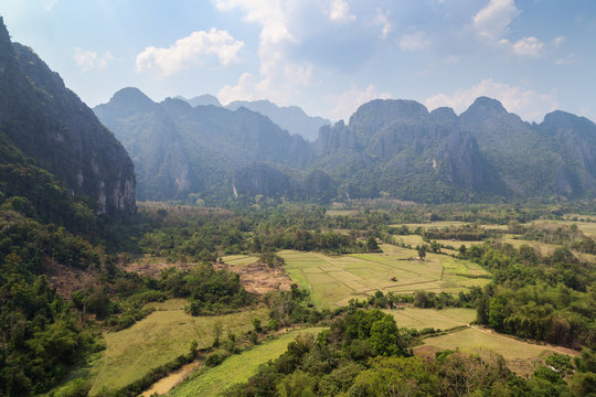 Beautiful view of fields and karst limestone mountains from above near Vang Vieng, Vientiane Province, Laos, on a sunny day.