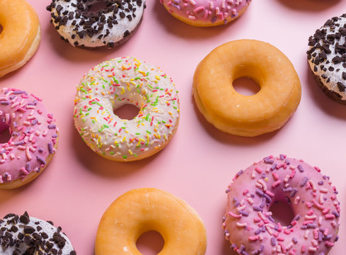 Top view of many colorful donuts on pink background.