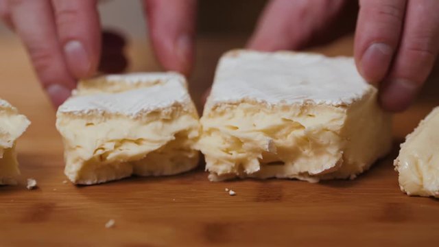 People cut cheese with a knife on old wooden table break brie close up macro cheese