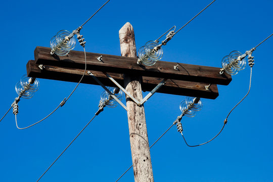 Old simple rural weathered wooden utility pole with parallel cables and insulators on blue sky