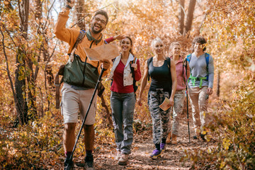 Man holding map and showing other hikers right way while walking in woods.