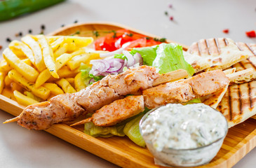 greek Chicken Souvlaki with salad, french fries potato, pita and tzatziki sauce on wooden plate