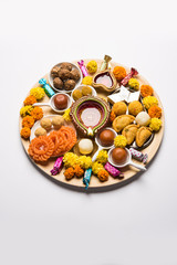 Diwali sweets arranged in a plate with diya and flowers