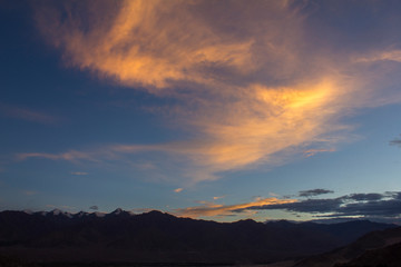 bright orange clouds in the evening sky over a mountain range with snowy peaks