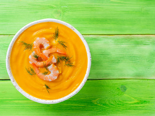Delicious yellow pumpkin cream soup with shrimp on bright green wooden table, top view, copy space