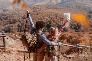 Couple hugging and holding arms raised with backs turned. In front of them mountain view.