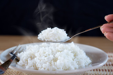 Asian woman eating cooked hot rice by spoon in a white plate 