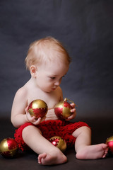 Fototapeta na wymiar The Concept Of The New Year. The Concept Of Christmas. Little boy baby sitting on a dark background and playing with Christmas balls