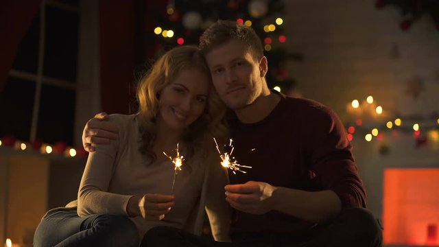 Sweet couple with Bengal lights sitting in cozy room near decorated X-mas tree