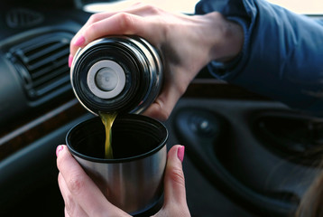 Fototapeta na wymiar Close-up woman's hands pouring a hot tea in a cup from thermos in the car in winter.