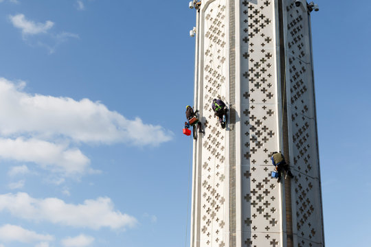 Three climbers repair the white high-rise monument landmark in Kyiv. Industrial climbers paint the facade of the of the white building with crosses