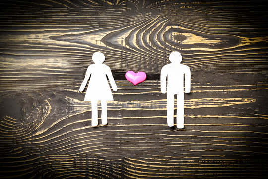 he and she are cut out of paper and in the middle a heart on a dark wooden background. illustration of the relationship between a devushka and a man.