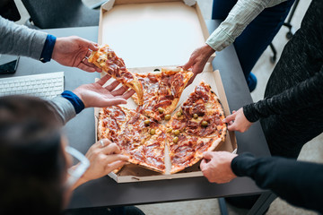 Close-up of a hands taking slices of pizza on a lunch break.