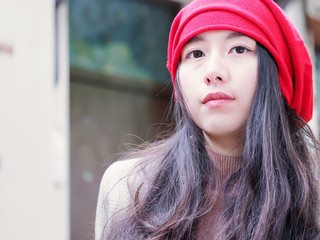 Beautiful young brunette woman in red headscarf sitting and looking aside daydreaming. Outdoor fashion portrait of glamour young Chinese stylish lady. Emotions, people, beauty and lifestyle concept.