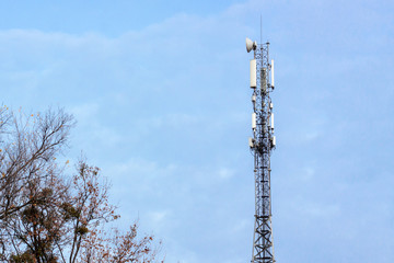 telecommunication tower on a background of tree and gloomy clouds