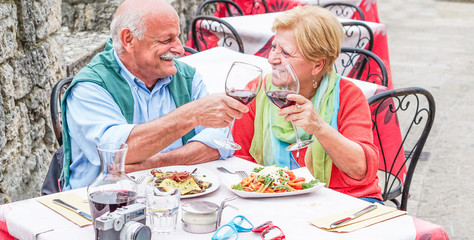 Retirement senior couple drinking and eating in restaurant outdoor - Mature husband and wife having fun in romantic vacation - Love, relationship and joyful elderly lifestyle concept