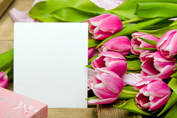 Pink tulip bouquet and sheet of paper on wooden background, copy space