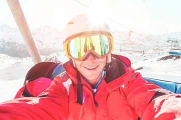 Fototapeta na wymiar Happy skier taking selfie photo with smartphone camera sitting on ski lift