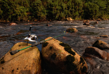 Ultralight fishing rod with a reel among mossy rocks on a tiny mountain river in Ireland