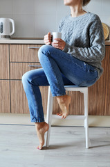 Cozy morning: beautiful young girl drinking coffee on a chair in the kitchen in the Scandinavian style.