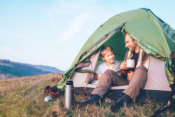 Father and son sit in camp tent drink hot tea and have conversation. Leisure time with father,...